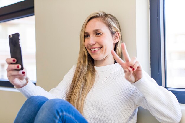 Photo young adult pretty blonde woman using her smartphone at home