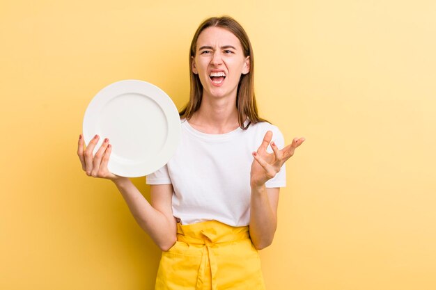 Foto cuoco unico della donna graziosa del giovane adulto con un piatto vuoto