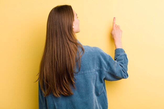 黄色の壁に隔離された若い大人のきれいな女性