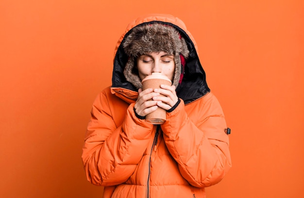 Young adult pretty woman wearing anorak and winter hat and holding a take away coffee