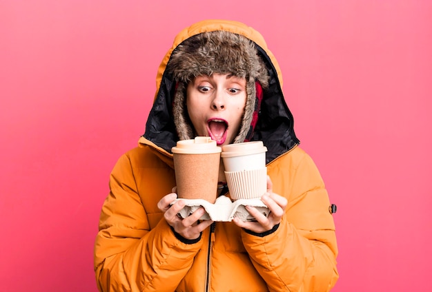 Giovane donna graziosa adulta che indossa giacca a vento e cappello invernale e tiene un caffè da asporto