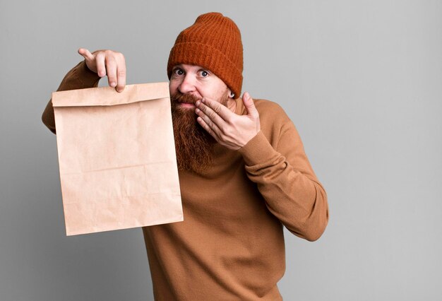 Young adult red hair bearded cool man with a paper bag with take away food