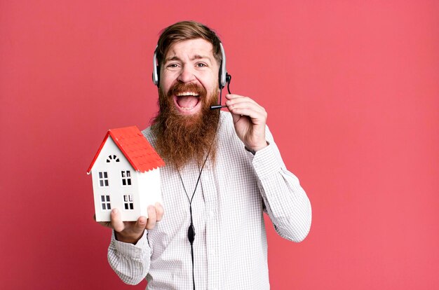 Молодой взрослый рыжеволосый бородатый крутой агент по недвижимости с моделью дома