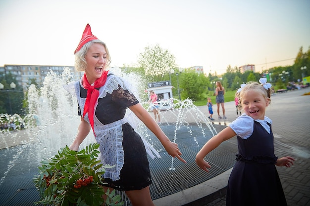Молодая и взрослая школьница в сентябре с цветами веселится возле воды фонтана поколения