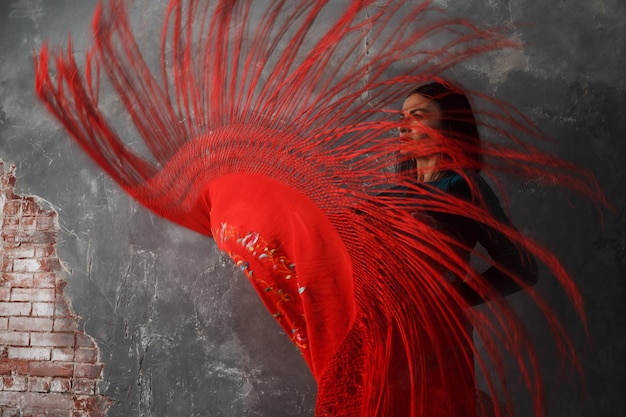 Young adult spanish woman dancing flamenco wth red shawl on\
gray vintage background