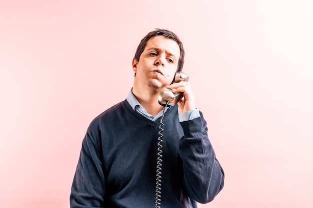 Photo young adult thirty five year old man in blue v-neck shirt and sweater with pink background talking on corded phone puffing from receiving bad news