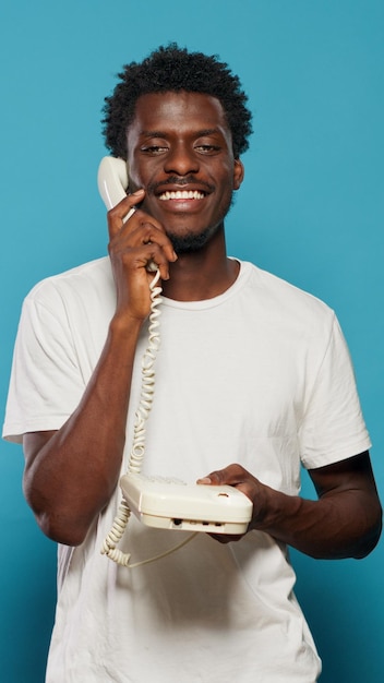 Young adult using landline telephone for phone call. Man talking on retro phone and smiling, using landline phone for communication. Modern person having fun and speaking on call