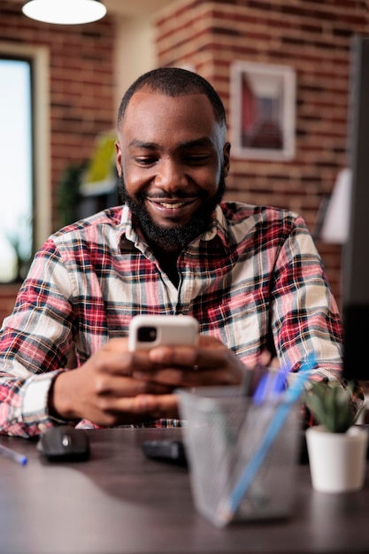 Giovane adulto che utilizza i social media sullo smartphone, lavora da remoto alla scrivania di casa. libero professionista che naviga sul sito web di internet sul telefono cellulare, seduto davanti al computer e naviga online sul web.