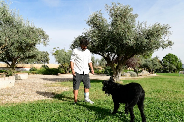 Young adult with a fractured foot and a walker boot playing with his pet, a black Schnauzer dog,