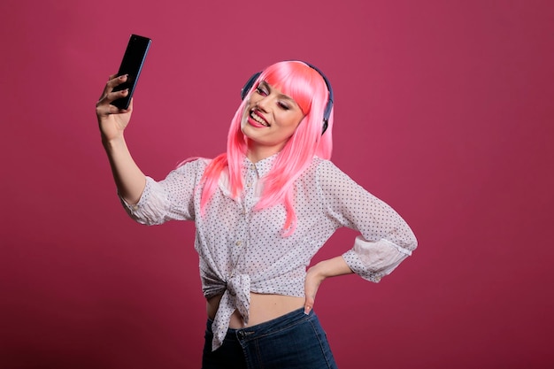 Young adult with pink hair taking pictures or recording video\
on smartphone, listening to music on headphones. using mobile phone\
to take photos and enjoy songs on headset for entertainment.