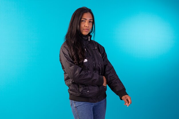 파란색 배경의 스튜디오 사진에서 검은 나일론 재킷을 입은 젊은 성인 여성