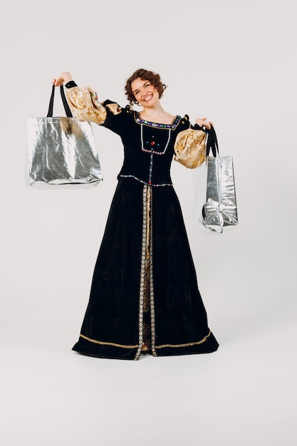사진 중세 드레스를 입은 젊은 성인 여성이 손에 쇼핑 가방을 들고 고립 된 색 배경