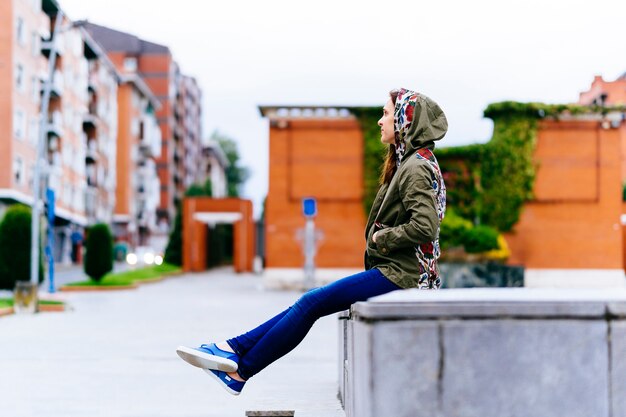 Young adult woman enjoying a cloudy day on the street in the city sitting in profile