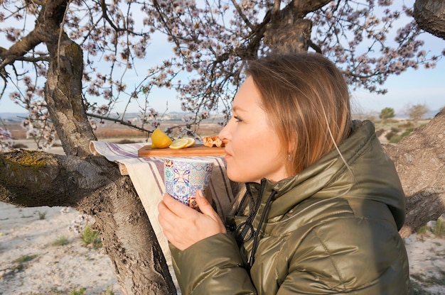 Foto giovane donna adulta che beve una bevanda calda alberi di mandorle in fiore all'aperto all'alba