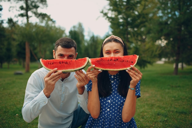 Giovane donna adulta e uomo coppia picnic al prato di erba verde nel parco divertendosi e sorridendo con l'anguria