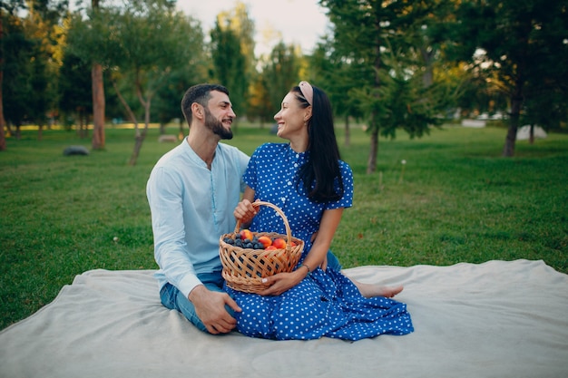 Giovane adulto donna e uomo coppia picnic seduto con cesto di frutta al prato di erba verde nel parco.