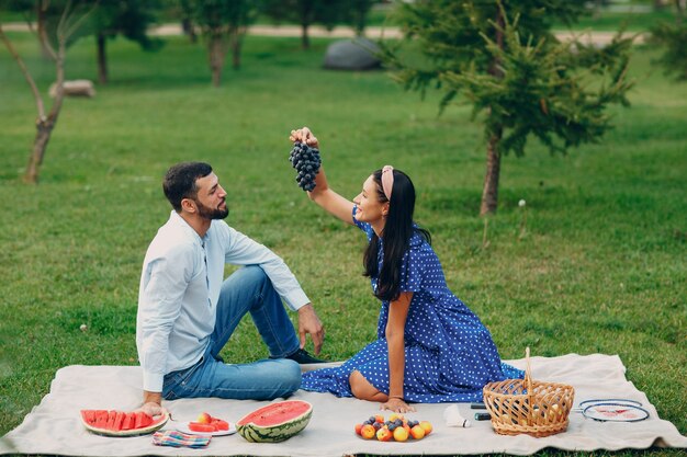 Young adult woman and man couple picnic with grape at green grass meadow in park