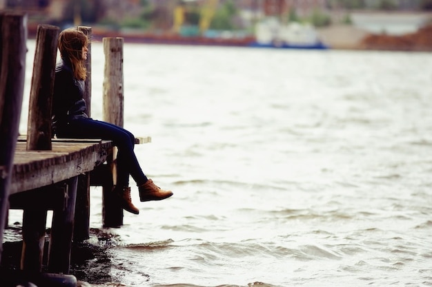 Young adult woman sitting on a wooden jetty on the river