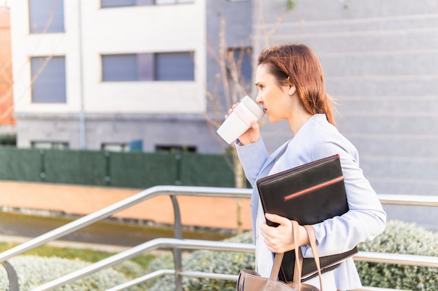 Giovane donna adulta sorridente bella imprenditrice lasciando lavorare con caffè per andare laptop e cartella. concetto di donna d'affari di successo