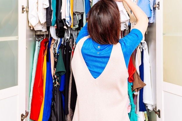 Young adult woman sorting out spring summer dresses in home dressing room