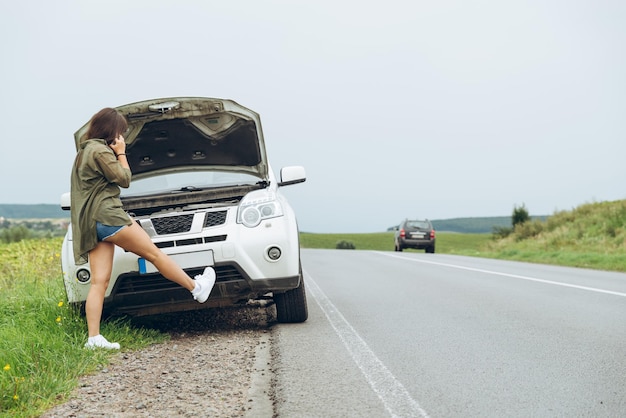 Young adult woman standing near broken car on highway and talkin