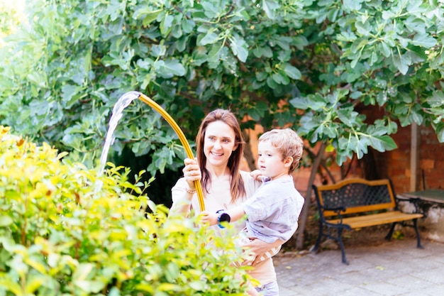 彼女の3歳の息子と一緒に庭に水をまく若い大人の女性