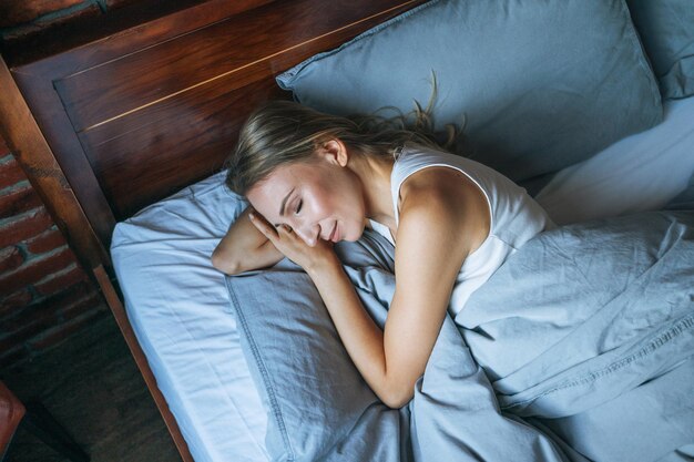 Young adult woman with blonde long hair sleeping on bed in loft room at the home