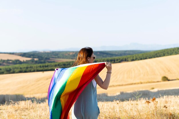 화창한 날 야외에서 LGBTIQ 깃발을 들고 자유를 느끼는 젊은 성인 여성