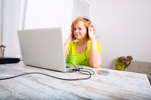 Young adult woman with headphones in front of a laptop	