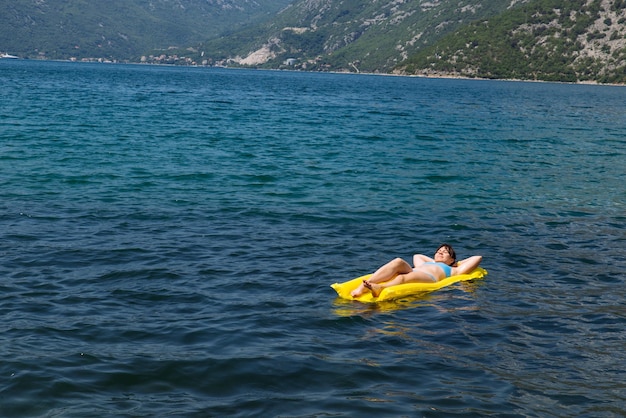 Young adult woman on yellow mattress in blue sea water