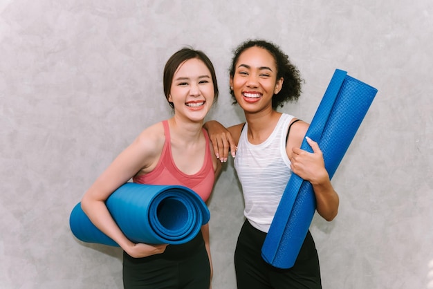 Молодые взрослые женщины с ковриком для йоги улыбаются и счастливы, тренируются дома с друзьями, концепция спорта и отдыха