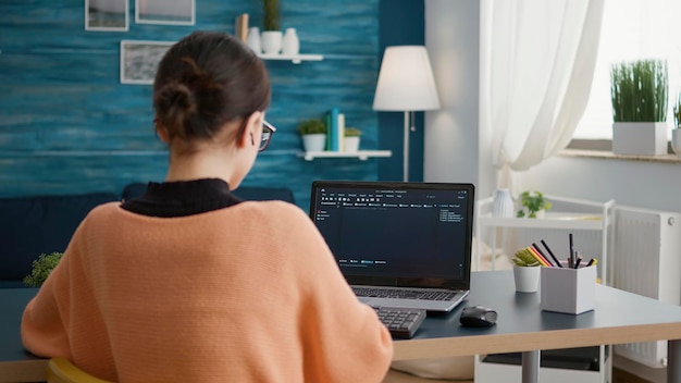 Young adult working on binary code programming at desk, using laptop with coding interface system. IT student using technical and economic data report to do remote engineer work.