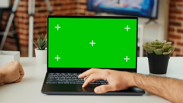 写真 デスクでグリーン スクリーン テンプレートを使用してラップトップで作業し、空白のクロマ キーとポータブル コンピューターの分離ディスプレイをチェックする若い成人。モックアップ copyspace で pc を見ています。三脚撮影。閉じる。