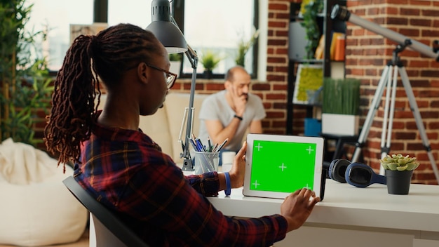 Молодой человек работает с горизонтальным зеленым экраном на беспроводном планшете, анализирует изолированный шаблон copyspace и фон макета. использование современного гаджета с пустым дисплеем хроматического ключа.