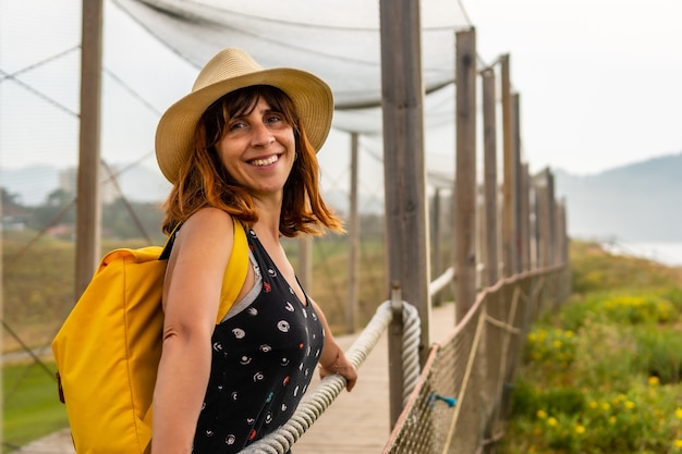 Foto giovane ragazza avventurosa con un cappello che guarda il mare da un sentiero sulla spiaggia