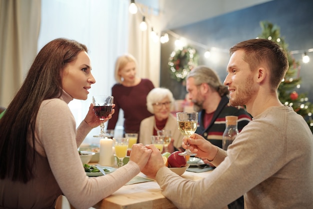 Young affectionate couple with glasses of wine making festive toast by served table