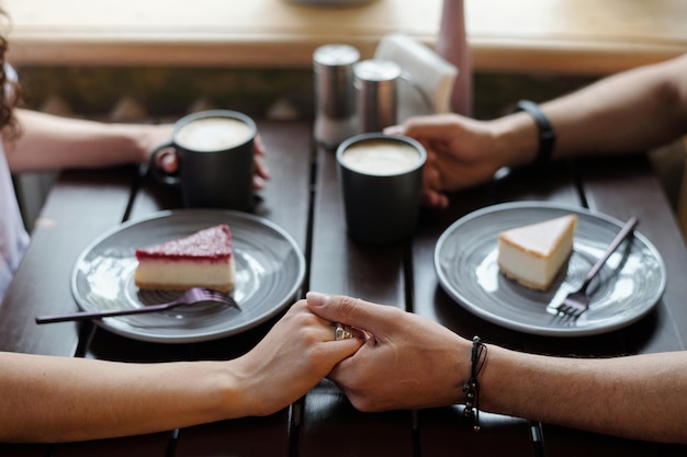 Young affectionate dates with cups of coffee holding by hands by table