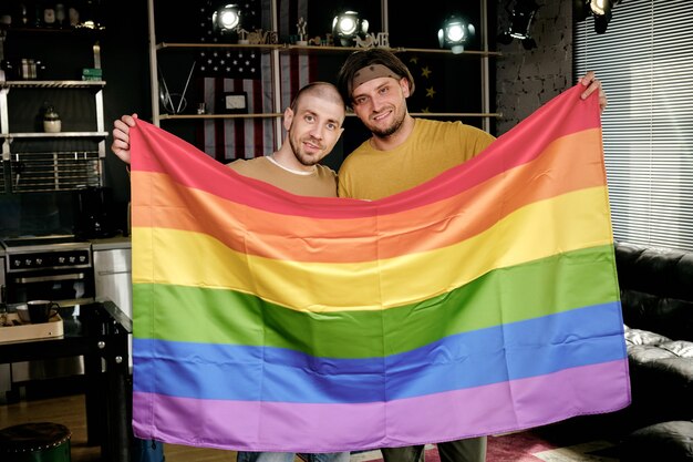 Photo young affectionate homosexual couple holding rainbow flag