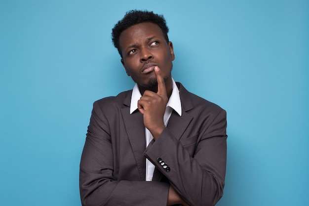 Young afrcain man in suit thinking on blue background