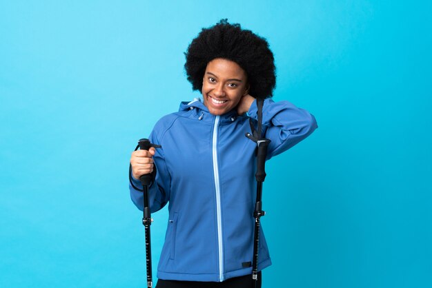 Young Africa American with backpack and trekking poles isolated on blue laughing