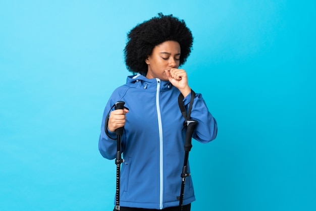 Young Africa American with backpack and trekking poles isolated on blue wall coughing a lot
