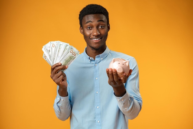 Young african amercian man holding piggy bank over yellow background