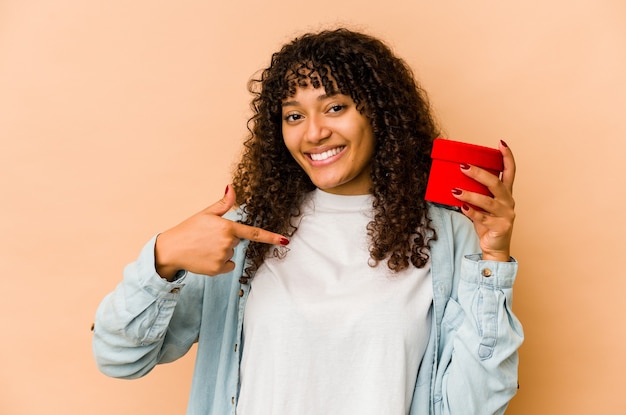 Young african american afro woman holding a valentines day gift person pointing by hand to a shirt copy space, proud and confident