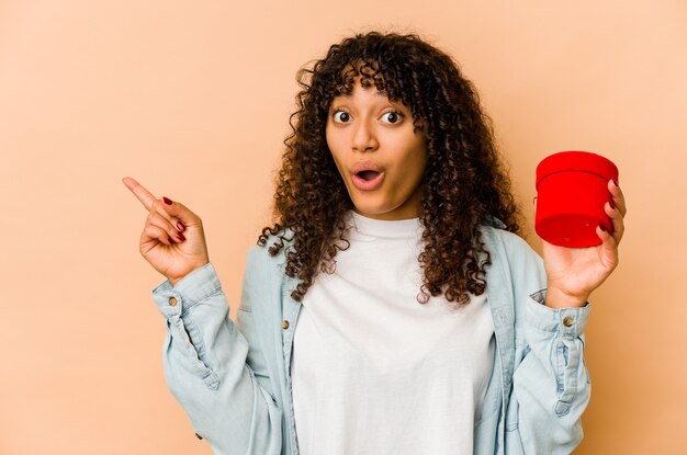 Young african american afro woman holding a valentines day gift pointing to the side