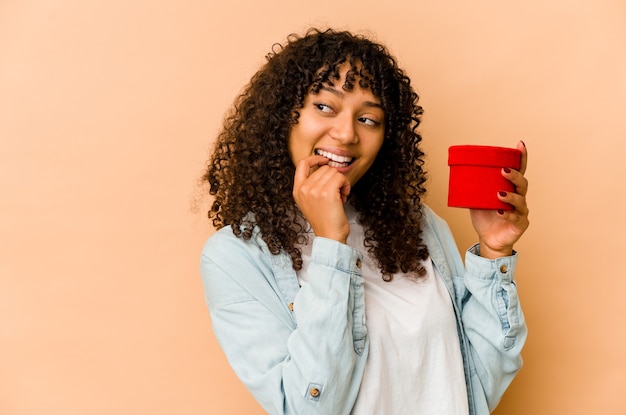 Young african american afro woman holding a valentines day gift relaxed thinking about something looking at a copy space.