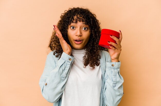 Young african american afro woman holding a valentines day gift surprised and shocked.