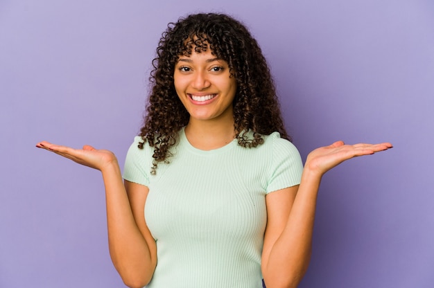 Young african american afro woman isolated makes scale with arms, feels happy and confident.