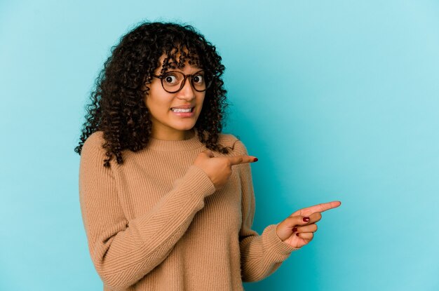 Giovane donna afroamericana afro isolata che punta scioccata con il dito indice a uno spazio di copia.