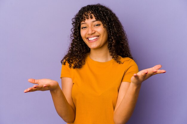 Young african american afro woman makes scale with arms, feels happy and confident.