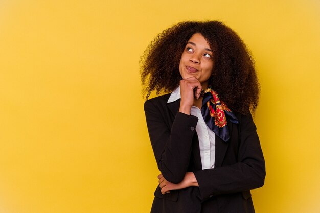 Young African American air hostess isolated on yellow background looking sideways with doubtful and skeptical expression.